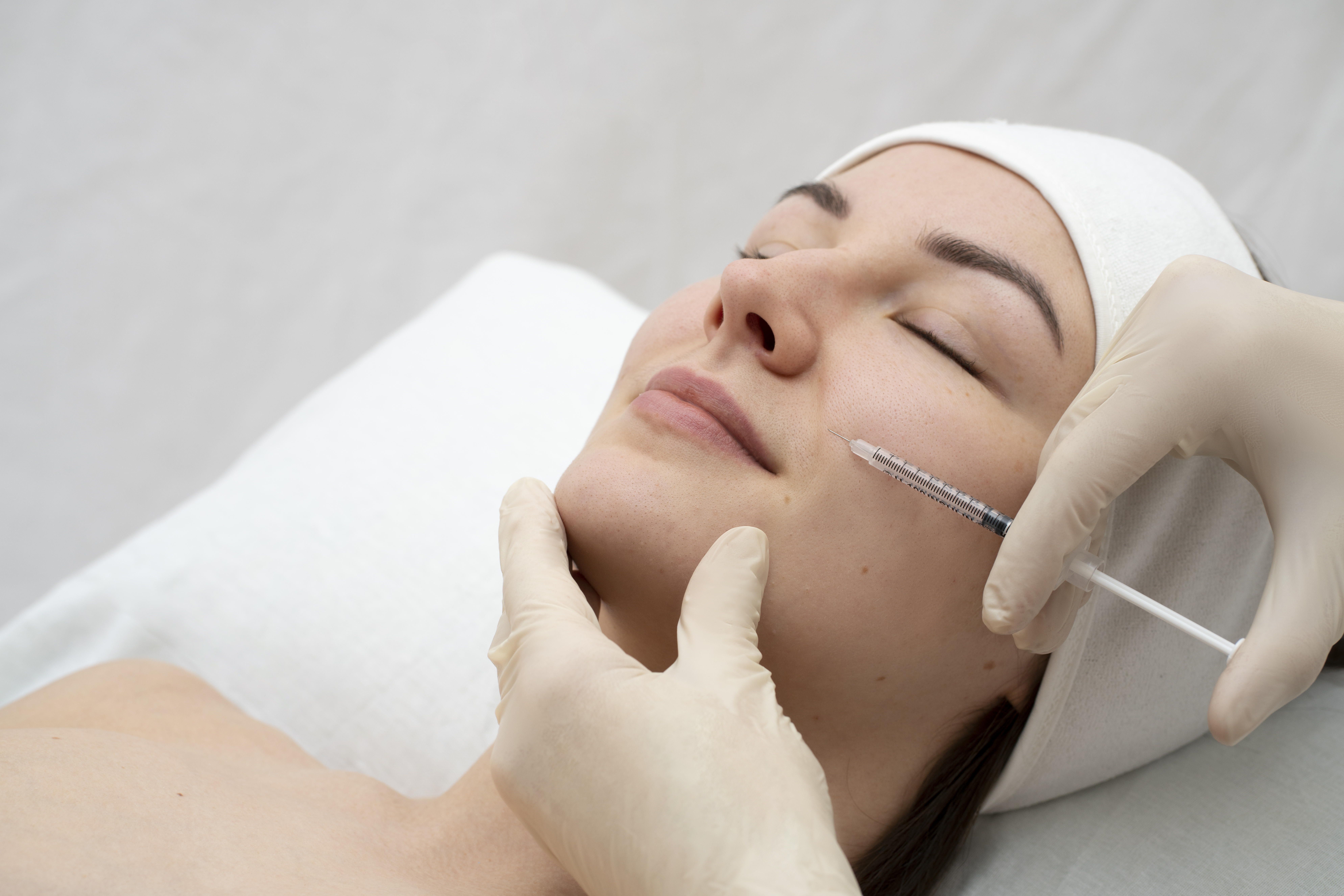 Profissional de saúde aplicando preenchimento com seringa no rosto de paciente durante procedimento de harmonização facial em clínica estética